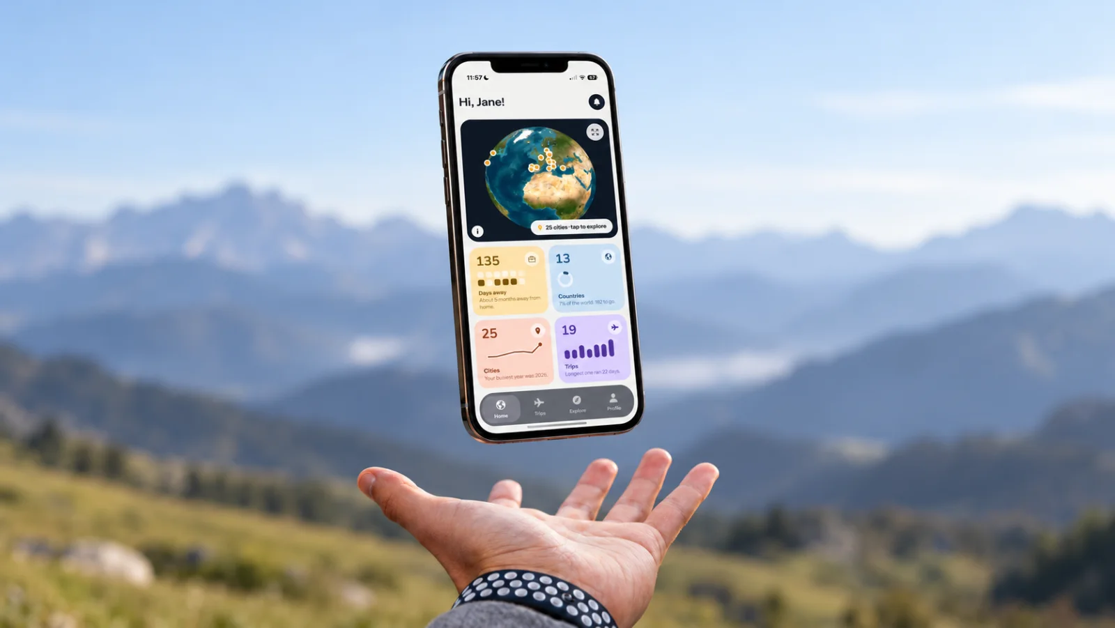 A hand reaching up to a floating phone that shows the TripsTracker home screen with its globe and travel statistics, mountains in the background